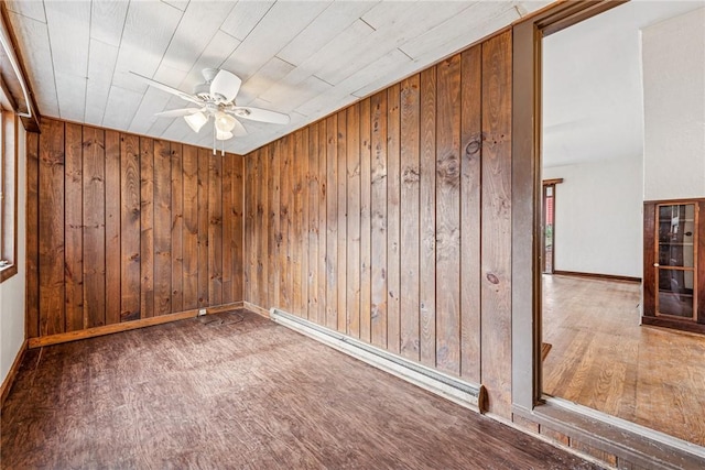 spare room featuring wooden walls, baseboards, a baseboard radiator, ceiling fan, and wood finished floors