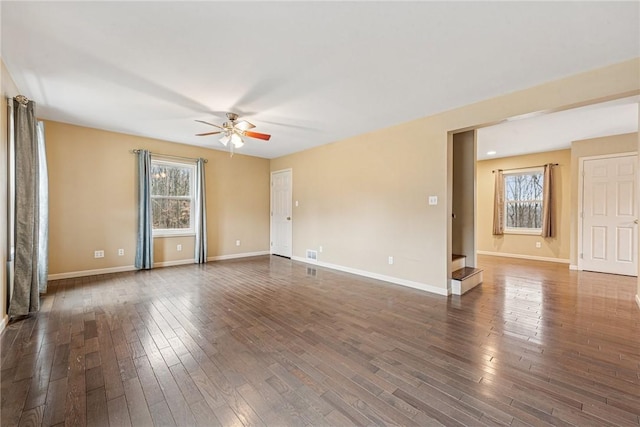 empty room with a ceiling fan, dark wood-style flooring, visible vents, and baseboards