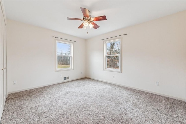 carpeted spare room with baseboards, visible vents, and ceiling fan