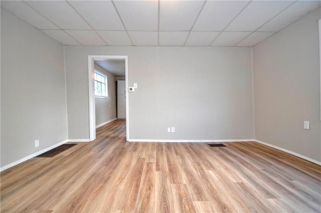 empty room with visible vents, light wood finished floors, a paneled ceiling, and baseboards