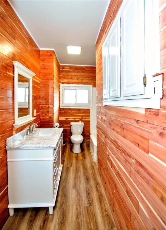 bathroom featuring a washtub, toilet, wood walls, vanity, and wood finished floors