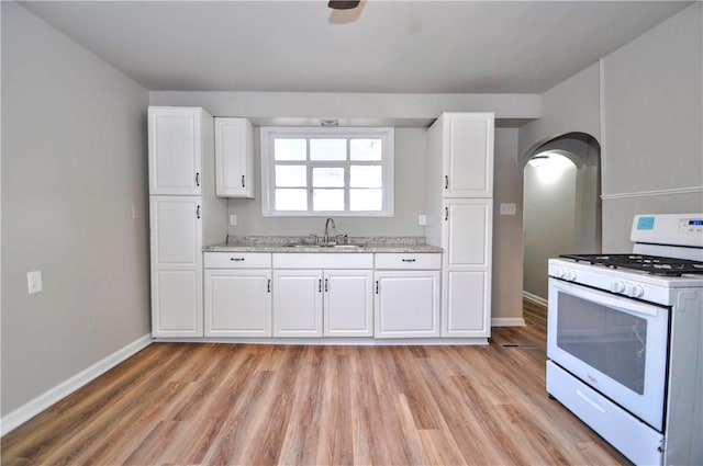 kitchen featuring light wood-type flooring, white cabinets, a sink, and white gas range oven