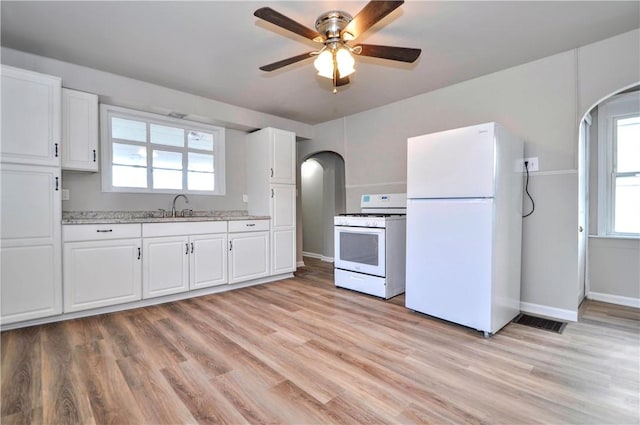 kitchen featuring white appliances, arched walkways, light wood-style floors, white cabinetry, and a sink