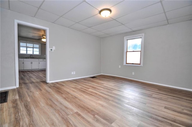 unfurnished room with a paneled ceiling, light wood-style flooring, and baseboards