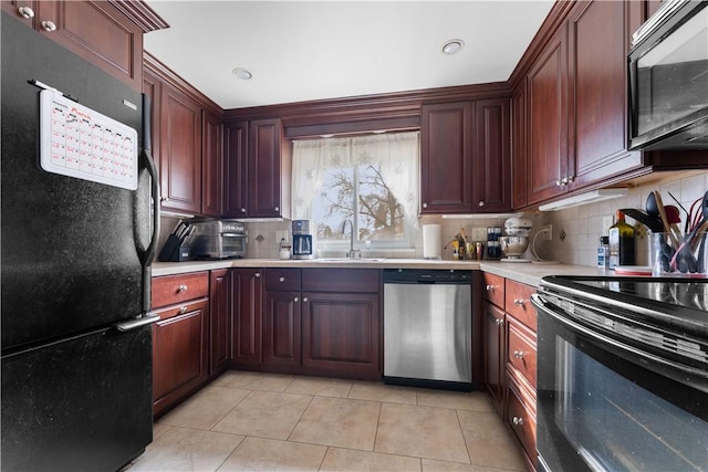 kitchen with light tile patterned floors, tasteful backsplash, light countertops, black appliances, and a sink