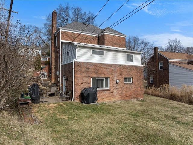 rear view of house featuring brick siding, a chimney, a patio area, and a lawn