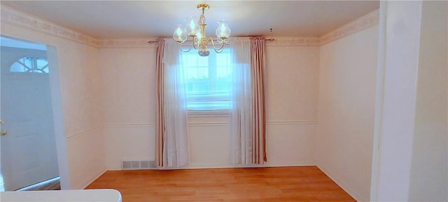 unfurnished room featuring visible vents, a notable chandelier, and wood finished floors