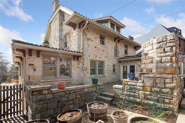 rear view of property featuring stone siding, a chimney, and fence