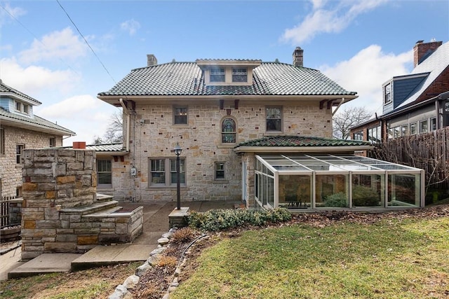 back of house with stone siding, a chimney, and a sunroom