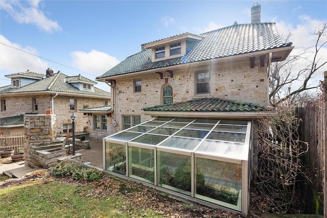 back of property with stone siding, a tiled roof, a chimney, and fence