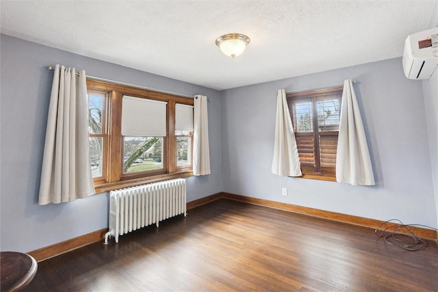 spare room featuring a wall mounted air conditioner, radiator heating unit, baseboards, and wood finished floors