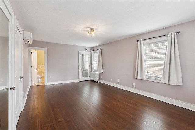 unfurnished bedroom featuring a wall unit AC, multiple windows, radiator, and dark wood-style flooring