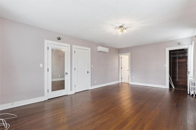 unfurnished room with radiator, a wall mounted air conditioner, baseboards, and wood finished floors