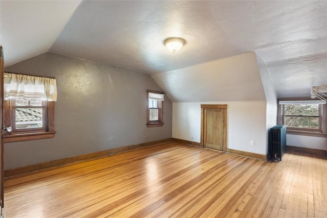 additional living space with hardwood / wood-style floors, radiator, a healthy amount of sunlight, baseboards, and lofted ceiling