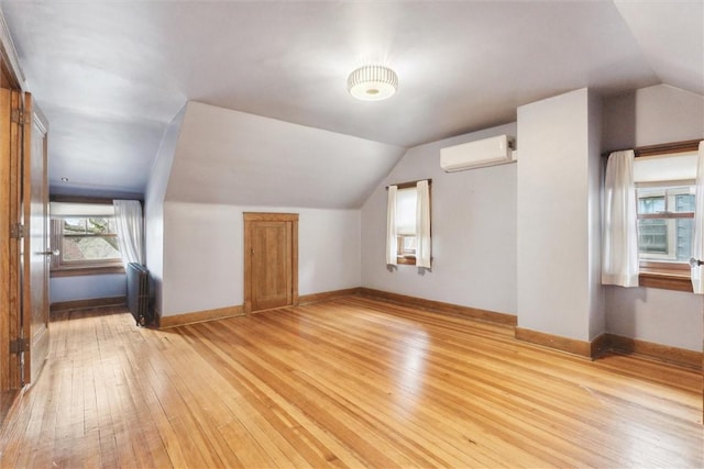 additional living space featuring light wood-type flooring, lofted ceiling, radiator heating unit, and a wall mounted AC