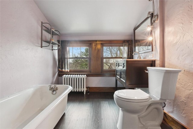 bathroom with wood finished floors, a soaking tub, radiator heating unit, toilet, and a textured wall