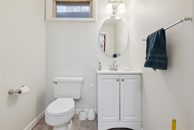 half bathroom featuring vanity, toilet, wood finished floors, and baseboards