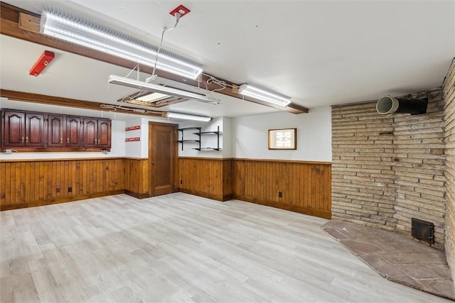 basement with light wood finished floors, a wainscoted wall, and wood walls