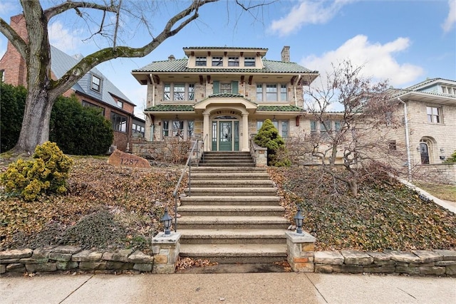 view of front of home featuring a tile roof, a balcony, stairway, and a chimney