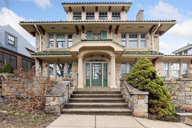 view of front of home featuring stone siding, a tiled roof, and a balcony