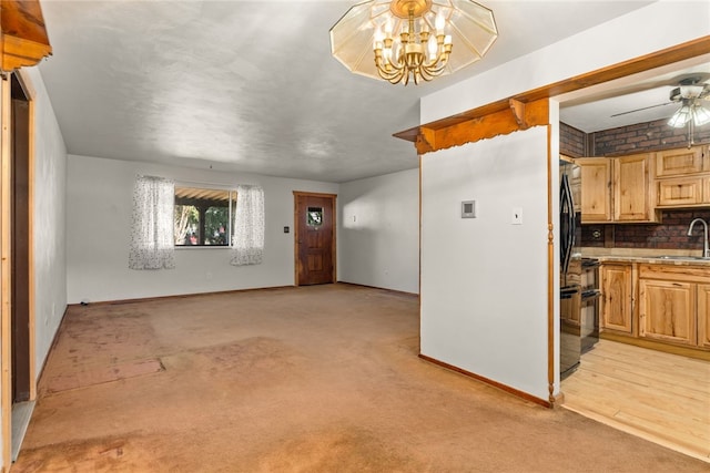 interior space with light carpet, baseboards, a sink, and ceiling fan with notable chandelier