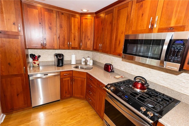 kitchen featuring stainless steel appliances, light wood-type flooring, brown cabinetry, and a sink