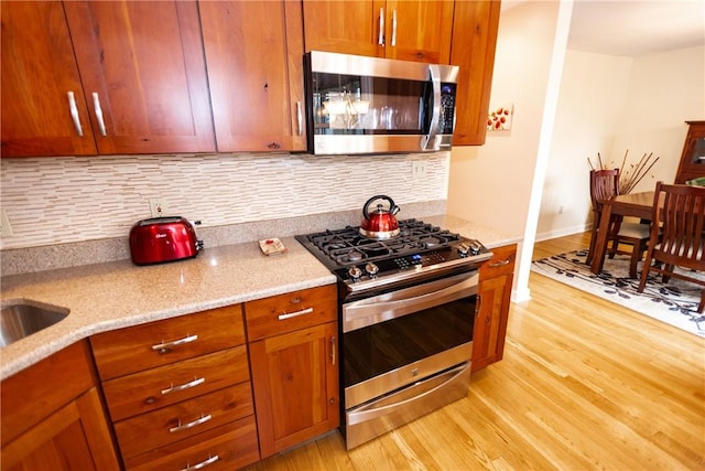 kitchen with appliances with stainless steel finishes, light wood-type flooring, light stone counters, and decorative backsplash