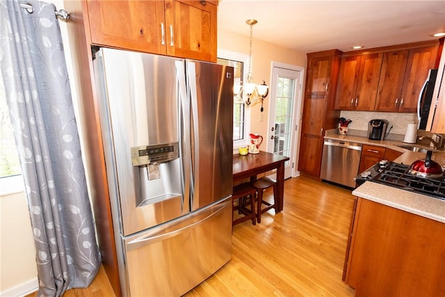 kitchen with backsplash, light wood-style flooring, appliances with stainless steel finishes, brown cabinetry, and a sink