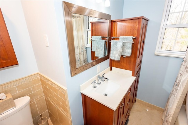 bathroom featuring a wainscoted wall, tile walls, toilet, vanity, and tile patterned flooring