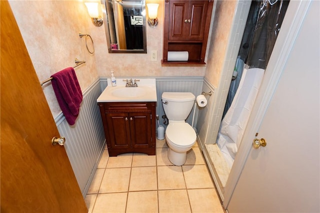 bathroom with wallpapered walls, wainscoting, toilet, tile patterned floors, and vanity