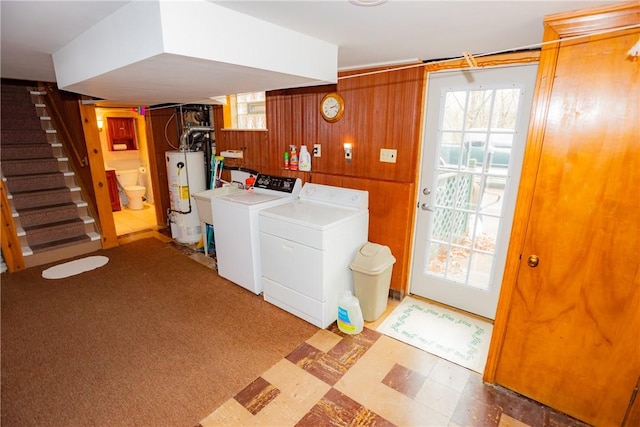 laundry room with plenty of natural light, washer and clothes dryer, tile patterned floors, wood walls, and gas water heater