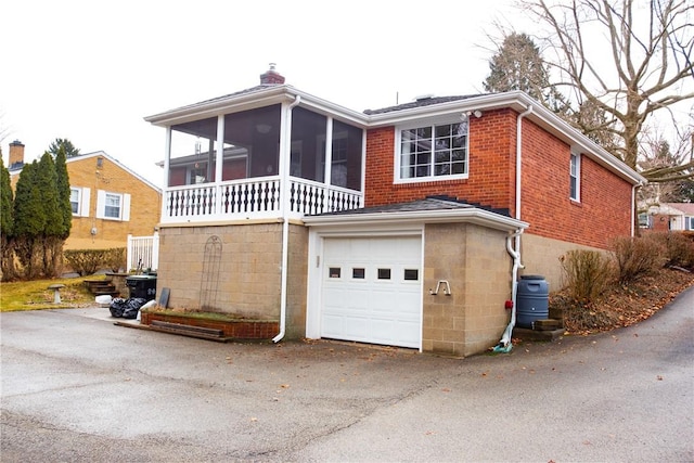 view of front of home with a sunroom, a chimney, aphalt driveway, an attached garage, and brick siding