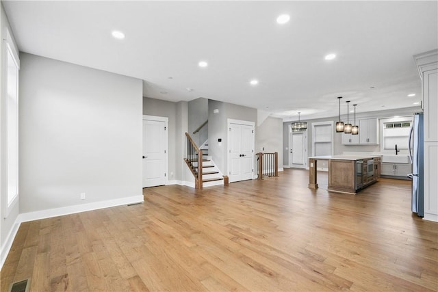 unfurnished living room featuring light wood-style floors, recessed lighting, visible vents, and stairway