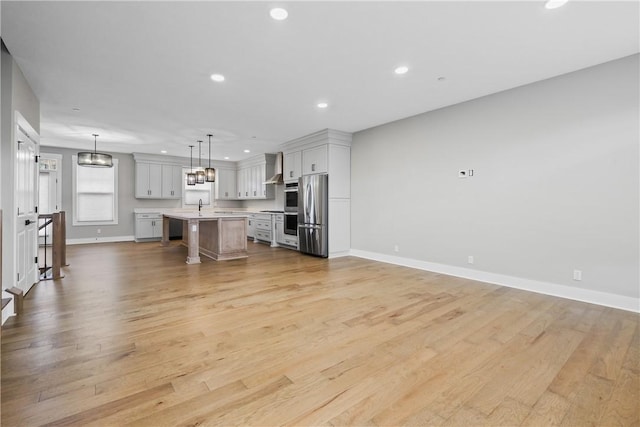 unfurnished living room with baseboards, light wood finished floors, a sink, and recessed lighting