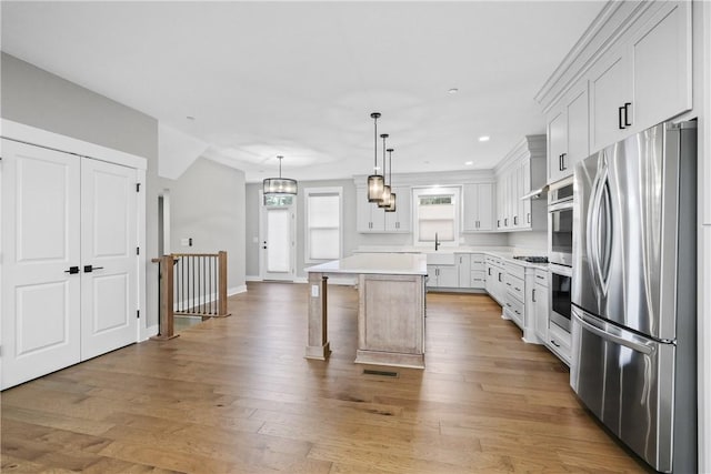 kitchen with stainless steel appliances, white cabinetry, light wood-style floors, a center island, and a kitchen bar