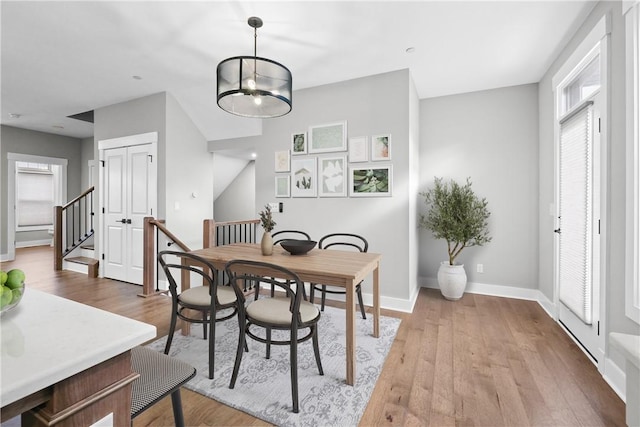 dining room with a notable chandelier, light wood-type flooring, stairs, and baseboards