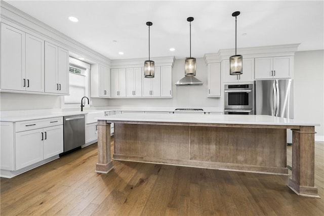 kitchen with hardwood / wood-style flooring, stainless steel appliances, light countertops, wall chimney range hood, and a center island