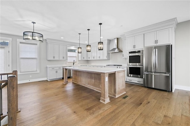 kitchen featuring light wood-style floors, light countertops, appliances with stainless steel finishes, wall chimney range hood, and a wealth of natural light