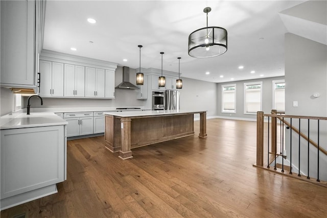 kitchen featuring a kitchen island, a sink, light countertops, dark wood-style floors, and wall chimney exhaust hood