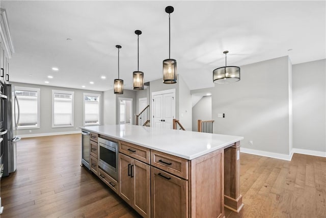 kitchen with light wood-style flooring, stainless steel microwave, light countertops, and baseboards