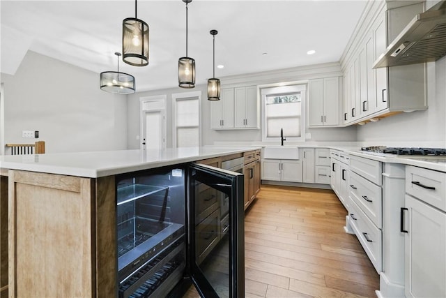 kitchen featuring wine cooler, light wood-style flooring, a kitchen island, light countertops, and wall chimney range hood