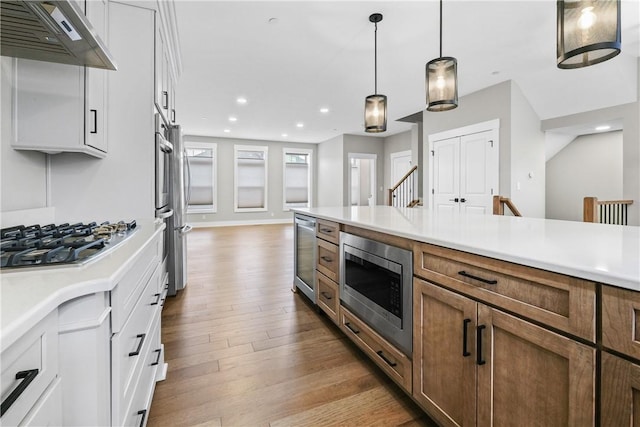 kitchen with wine cooler, light countertops, appliances with stainless steel finishes, under cabinet range hood, and hardwood / wood-style floors