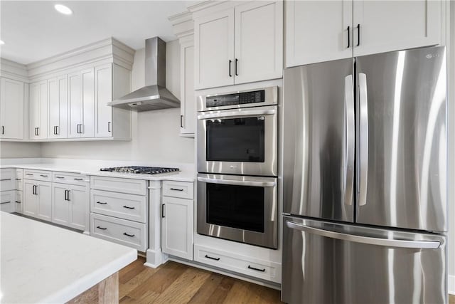 kitchen with dark wood finished floors, light countertops, appliances with stainless steel finishes, white cabinets, and wall chimney range hood