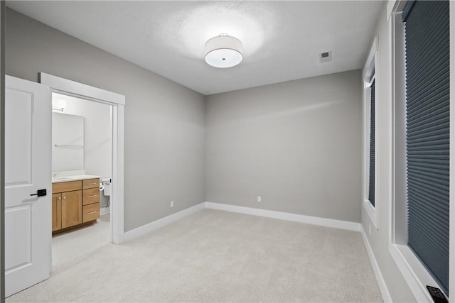 unfurnished bedroom featuring light colored carpet, connected bathroom, visible vents, and baseboards