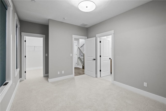 unfurnished bedroom with a spacious closet, a closet, carpet flooring, and baseboards