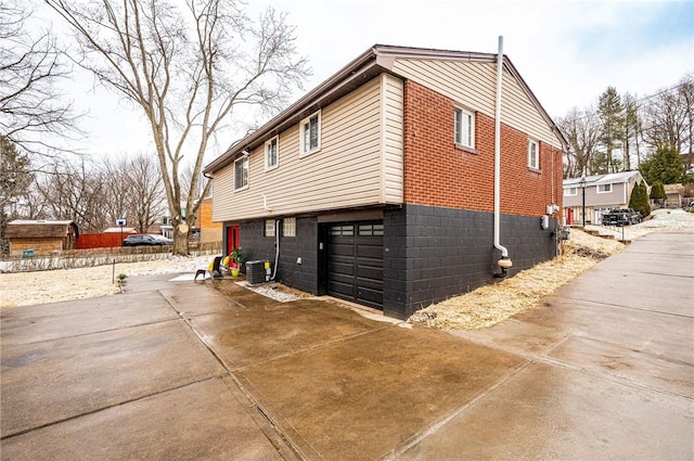 view of side of property with a garage, cooling unit, concrete driveway, and brick siding