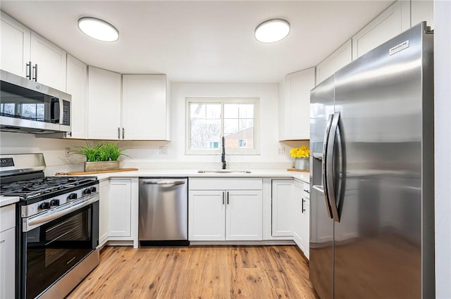 kitchen with stainless steel appliances, a sink, white cabinets, light countertops, and light wood-type flooring