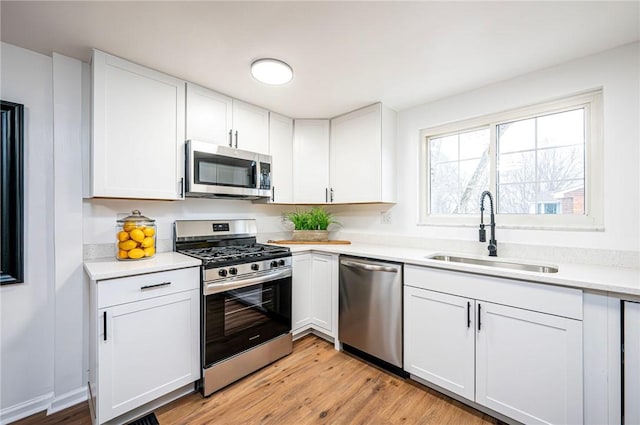 kitchen featuring stainless steel appliances, light countertops, light wood-style floors, white cabinets, and a sink