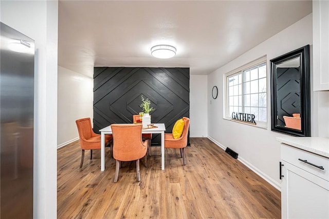 dining room with light wood finished floors, an accent wall, and baseboards