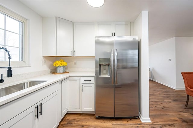 kitchen with light countertops, light wood-style floors, white cabinets, a sink, and stainless steel fridge with ice dispenser